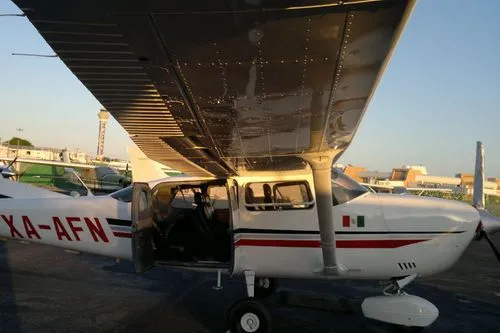 Bílé malé letadlo Cessna s otevřenými dveřmi zaparkované na letišti za soumraku.