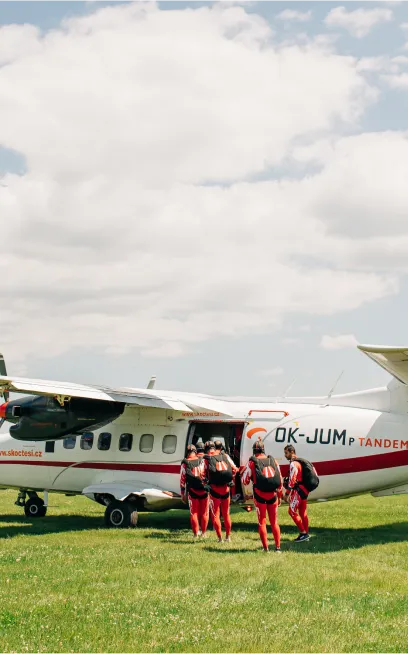 Tandem pilot s pasažéry nastupující do letadla před tandemovým seskokem