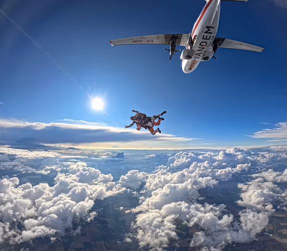tandem jump from afar with clouds and an aircraft